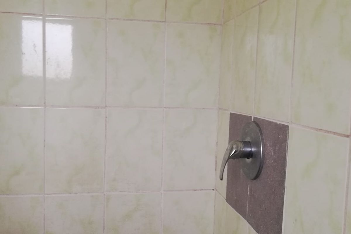 A close-up view of a shower area featuring dated ceramic wall tiles and a standard chrome shower mixer tap.
