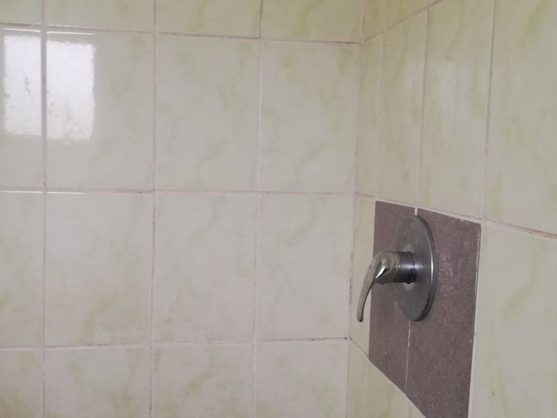 A close-up view of a shower area featuring dated ceramic wall tiles and a standard chrome shower mixer tap.