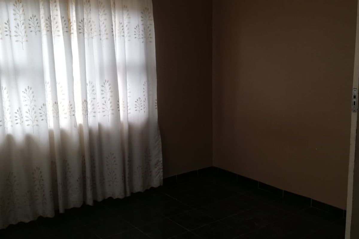 An empty bedroom featuring dark tiled flooring and neutral wall paint, providing a blank canvas for potential interior design updates.