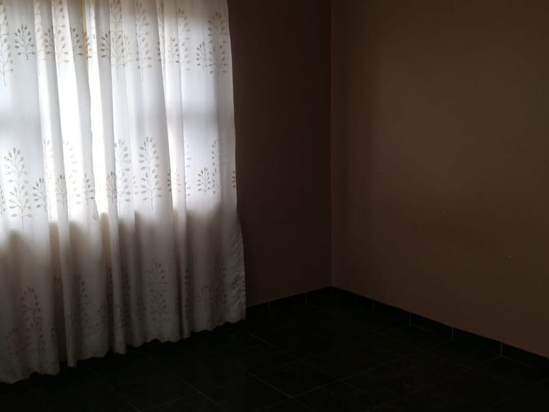 An empty bedroom featuring dark tiled flooring and neutral wall paint, providing a blank canvas for potential interior design updates.
