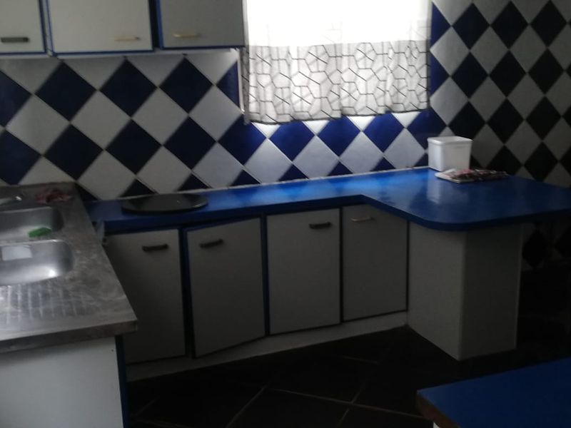 A dated kitchen featuring blue and white diamond-patterned wall tiles, laminate countertops, and built-in cabinetry with a double bowl stainless steel sink.