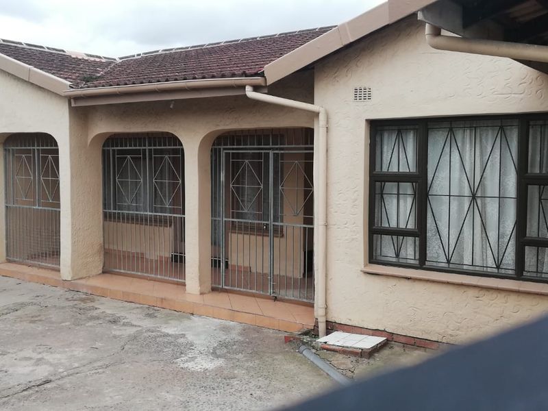 Rear exterior view of the house featuring a tiled roof, security gates on the patio area, and a concrete driveway.