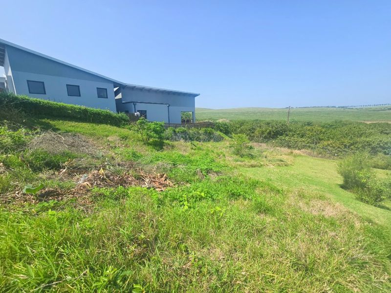 A view of the rear garden area featuring a sloped lawn, retaining wall, and perimeter fencing, adjacent to the side elevation of the residence.
