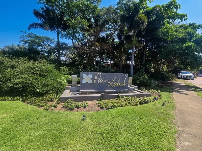 The entrance to Palm Lakes estate featuring a modern stone signage monument, integrated water feature, and well-maintained landscaped gardens.