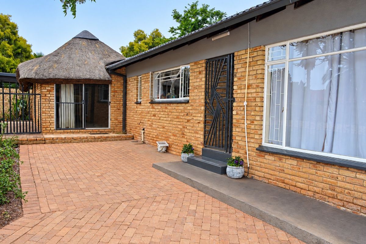 Rear exterior view featuring a face brick facade, a paved courtyard area, and a unique thatched roof section with secure access points.