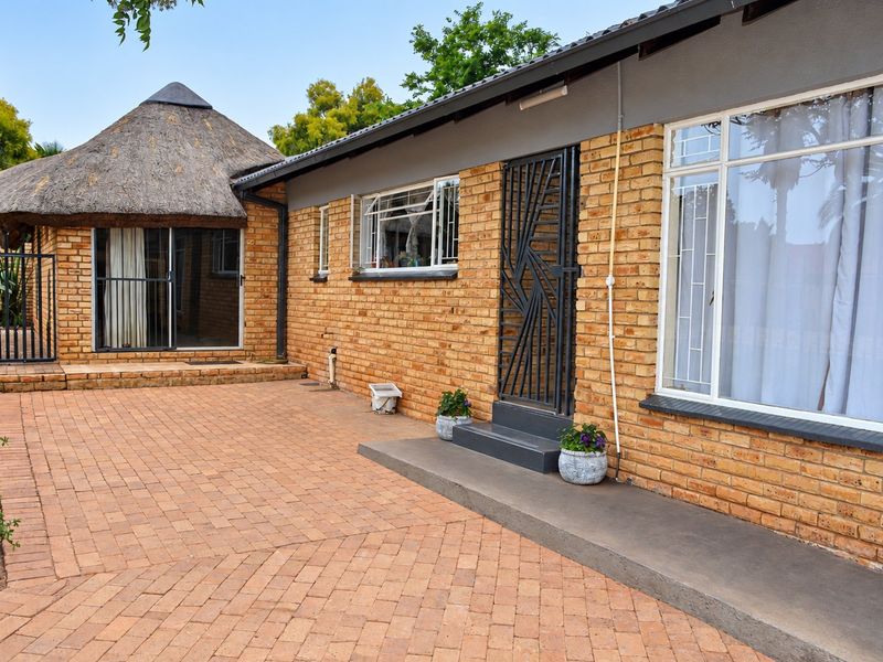 Rear exterior view featuring a face brick facade, a paved courtyard area, and a unique thatched roof section with secure access points.