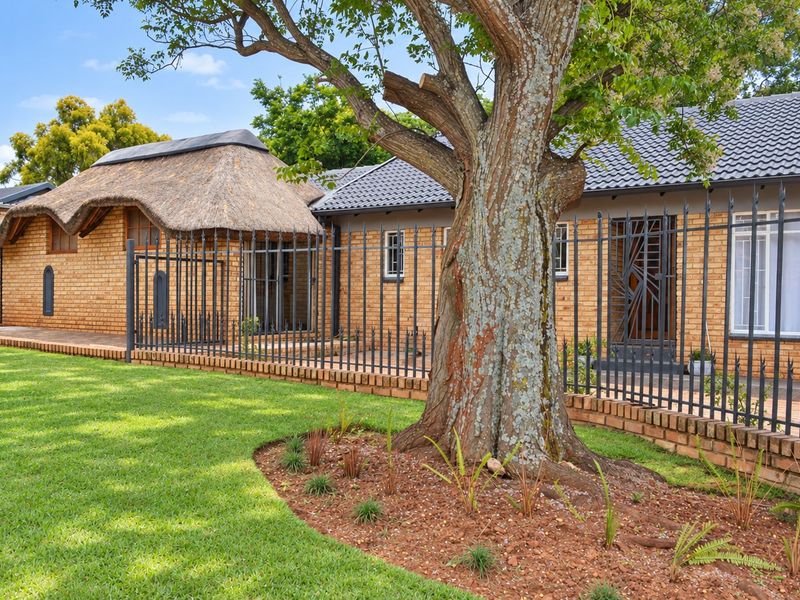 Front view of a charming face brick house featuring a combination of thatched and tiled roofing, secured by wrought iron fencing and a landscaped garden.