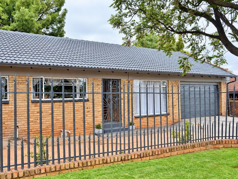 Front view of a single-story face brick house featuring a tiled roof, secure metal fencing, and an integrated garage.