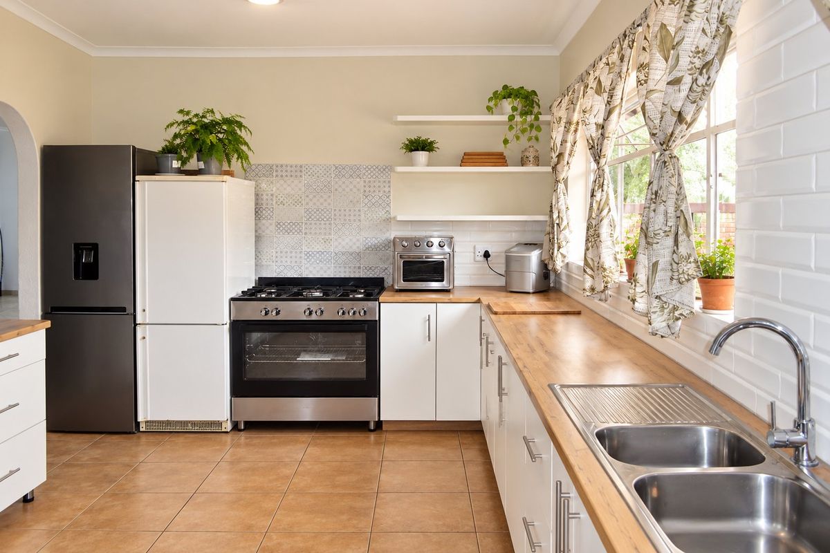 A well-maintained kitchen featuring a gas stove, oven, double sink with mixer tap, wooden countertops, and ample built-in cabinetry with floating shelves.