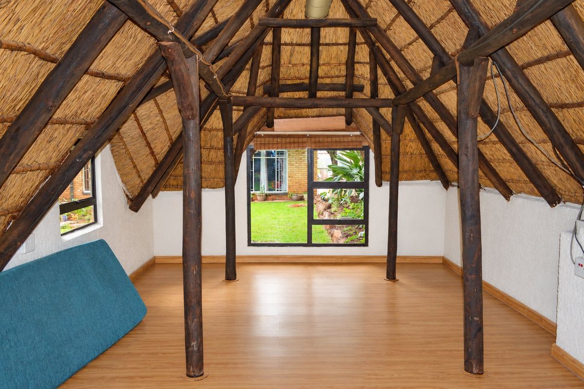Spacious attic-style bedroom featuring exposed timber rafters, a traditional thatched roof, laminate flooring, and large windows overlooking the garden.