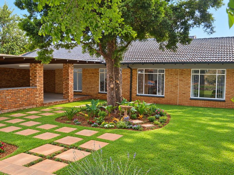 A well-maintained rear exterior view featuring a face brick facade, a covered patio area, and a neatly landscaped garden with a paved walkway.