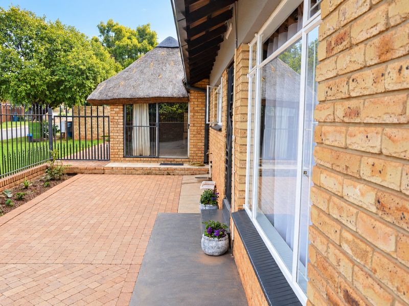 A view of the rear exterior featuring brick paving, a thatched roof structure, and secure metal fencing along the property boundary.