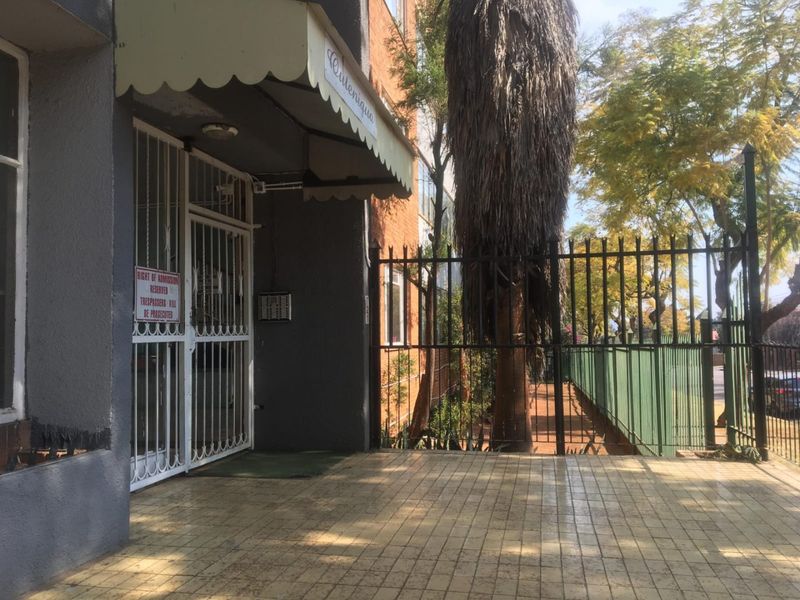 The apartment building entrance features a tiled walkway, security gate, and protective awning, providing a secure and functional access point to the property.