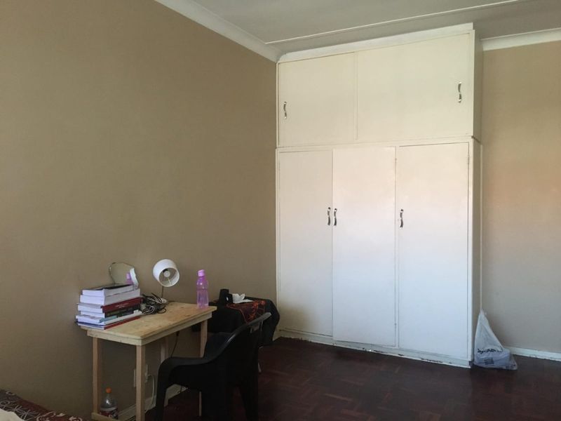 A bedroom featuring classic parquet flooring and floor-to-ceiling built-in cupboards, offering practical storage space within a neutral-toned room.