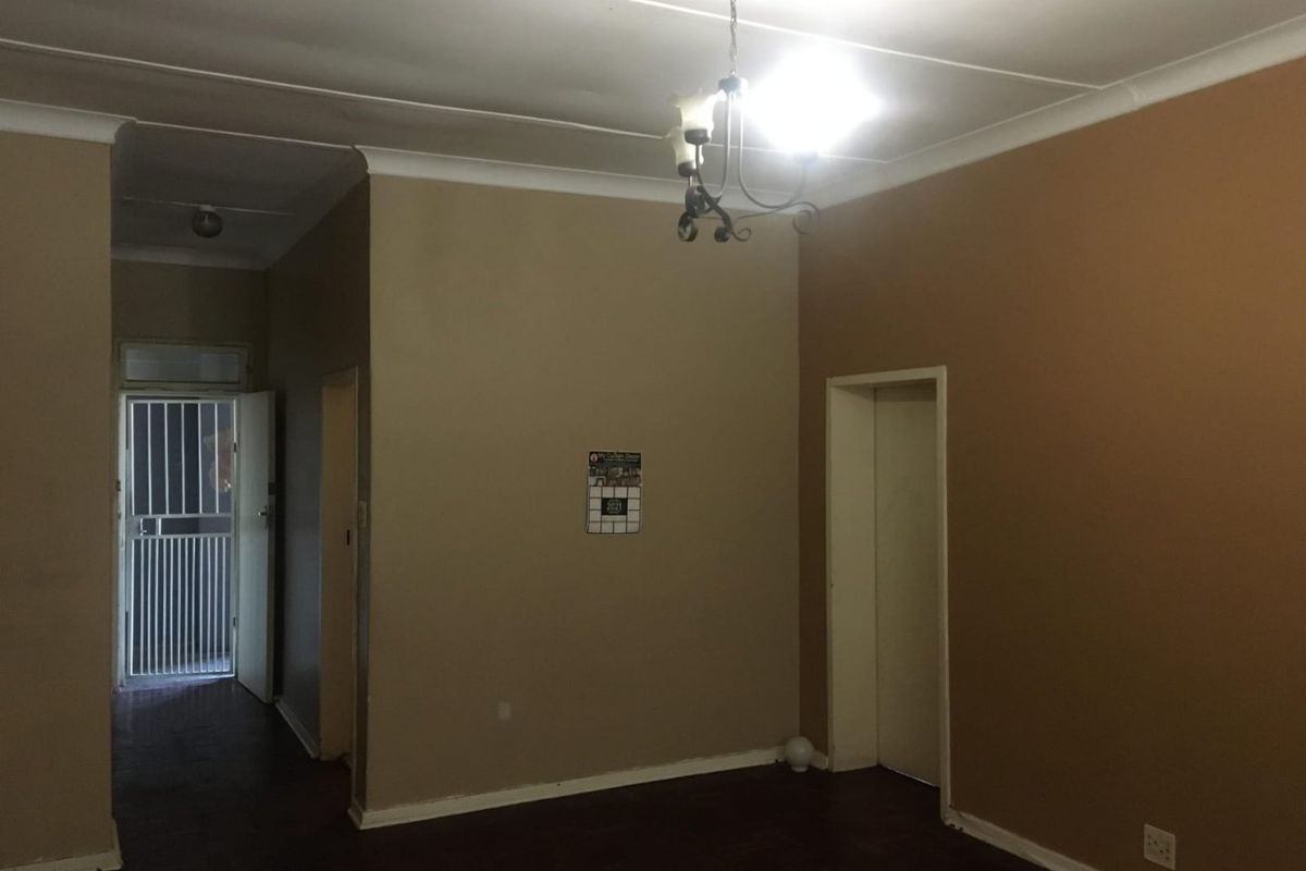 An empty living room featuring parquet flooring, cove cornicing, and a security gate at the entrance, offering a blank canvas for renovation.