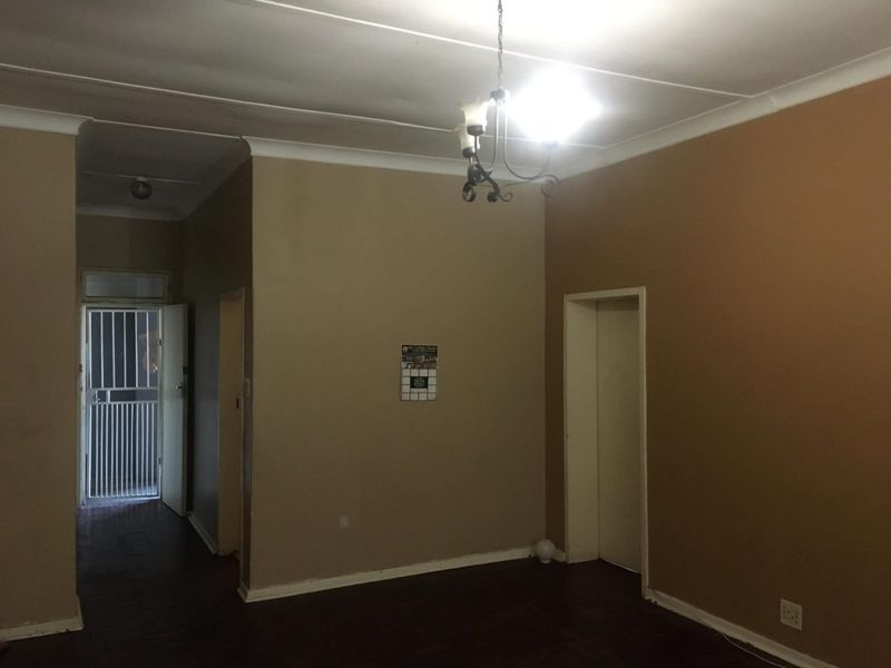 An empty living room featuring parquet flooring, cove cornicing, and a security gate at the entrance, offering a blank canvas for renovation.
