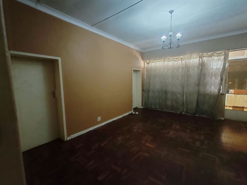 An empty living room featuring dark parquet flooring, coved ceilings, and a central light fixture, offering a blank canvas for renovation.