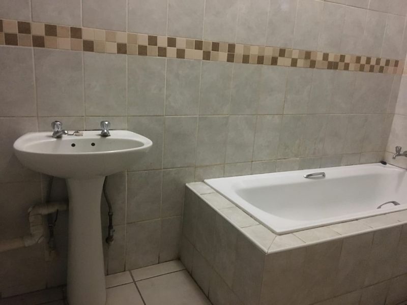 A dated bathroom featuring a pedestal basin and a built-in bathtub with tiled surround and decorative accent border.