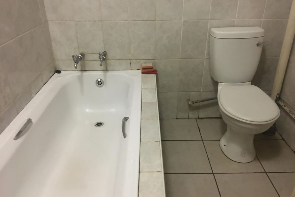 A functional bathroom featuring a standard bathtub and toilet with tiled wall and floor finishes, requiring cosmetic updates to improve its overall condition.