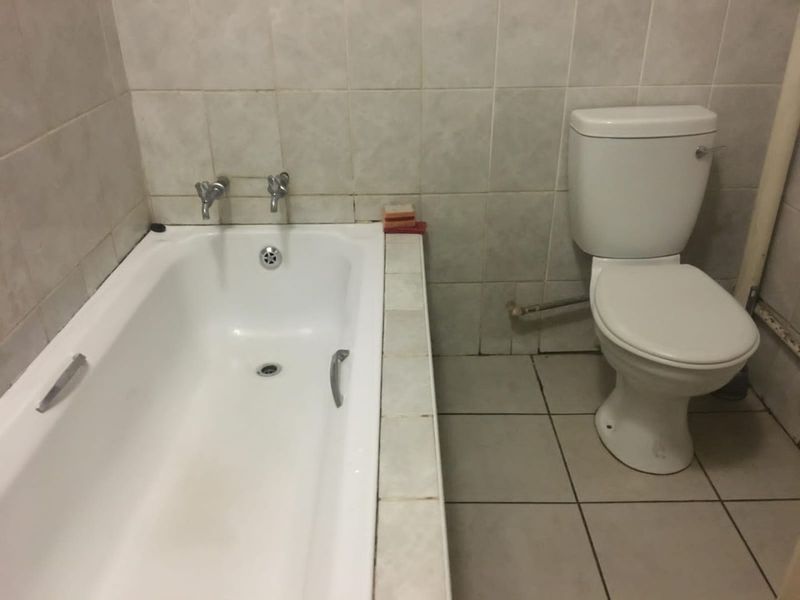 A functional bathroom featuring a standard bathtub and toilet with tiled wall and floor finishes, requiring cosmetic updates to improve its overall condition.