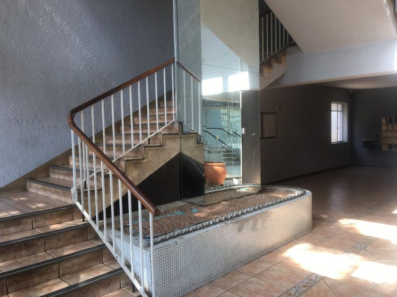 Spacious apartment building entrance lobby featuring a central staircase with metal balustrades and a decorative tiled planter box with a mirrored feature wall.