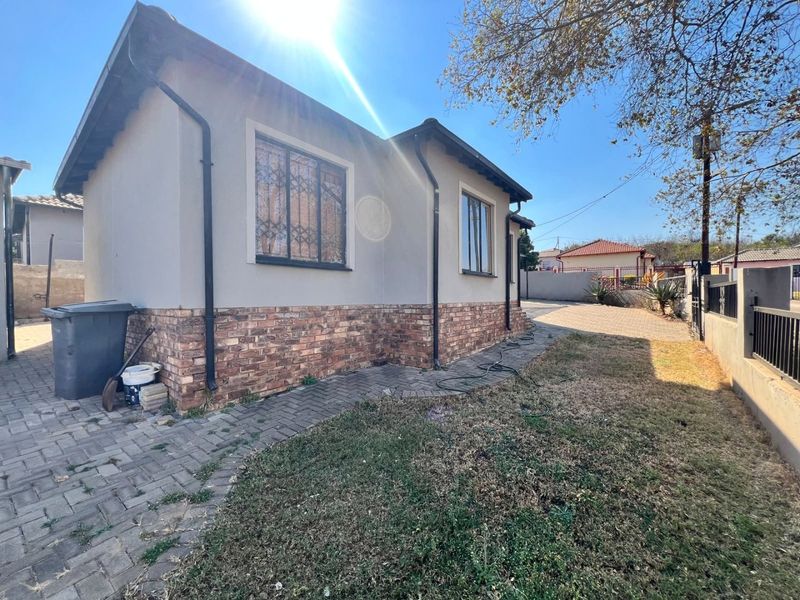 Rear view of the house featuring a brick-base facade, plastered walls, security-barred windows, and a paved walkway leading through the garden area.