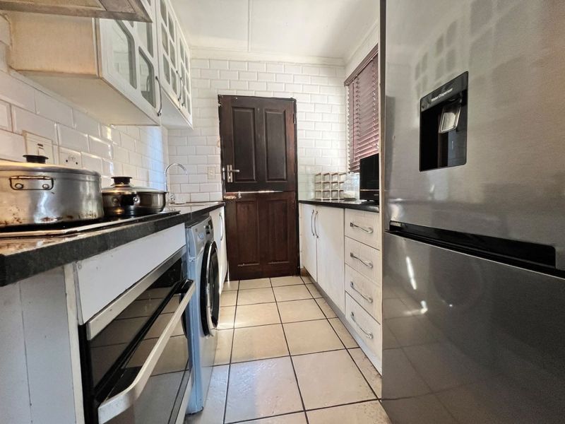 A functional galley-style kitchen featuring white cabinetry, subway tile backsplash, tiled flooring, and a stable door leading to the exterior.