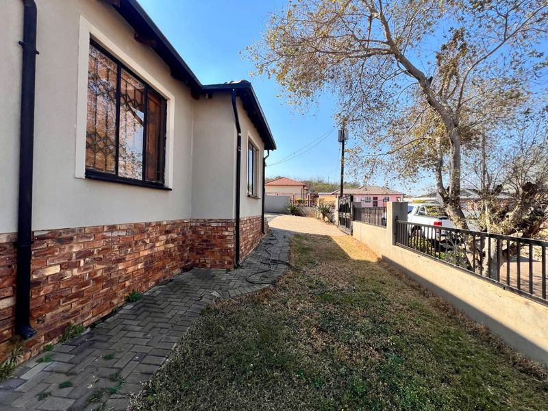 Side view of the property featuring a brick-clad lower facade, paved walkway, and metal perimeter fencing along the boundary.