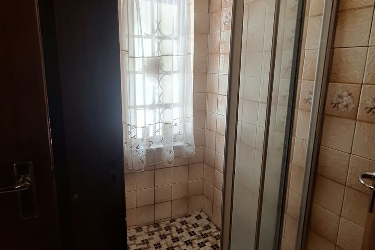 A compact bathroom featuring a shower enclosure with sliding glass doors, tiled walls, and patterned floor tiles.