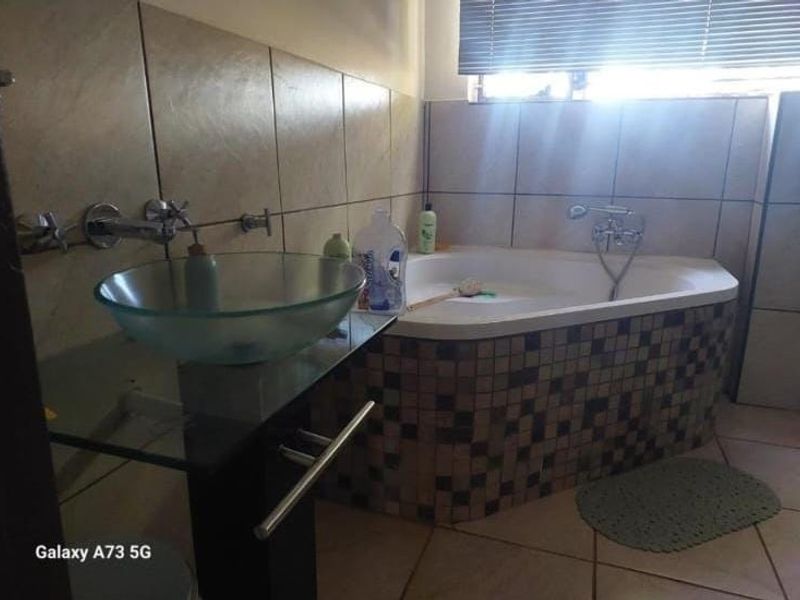 Bathroom featuring a corner bathtub with mosaic tile surround, a glass vessel sink with wall-mounted hardware, and neutral ceramic wall tiling.