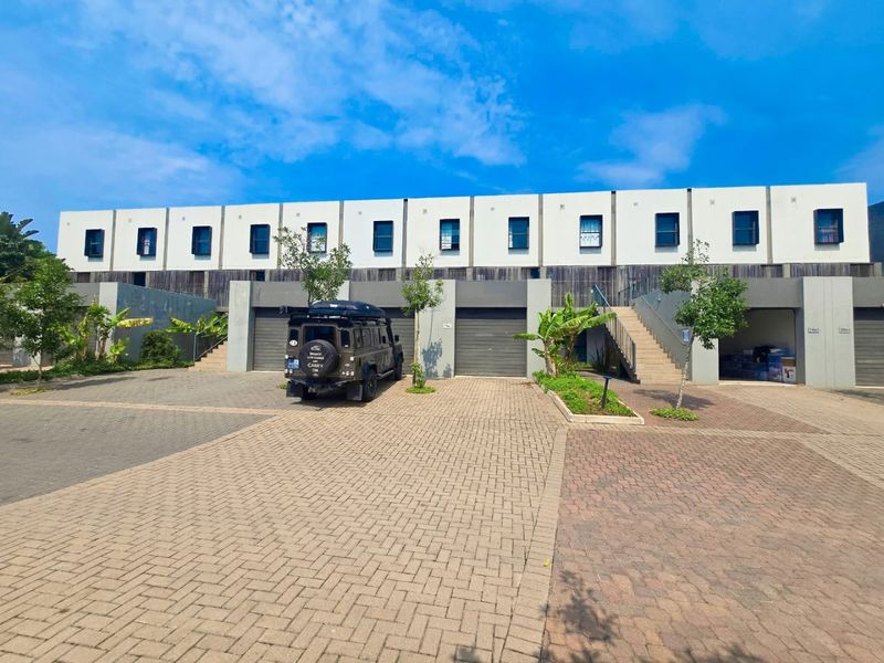 Front elevation of a modern apartment complex featuring paved driveway access, multiple garage units, and external staircases leading to upper levels.