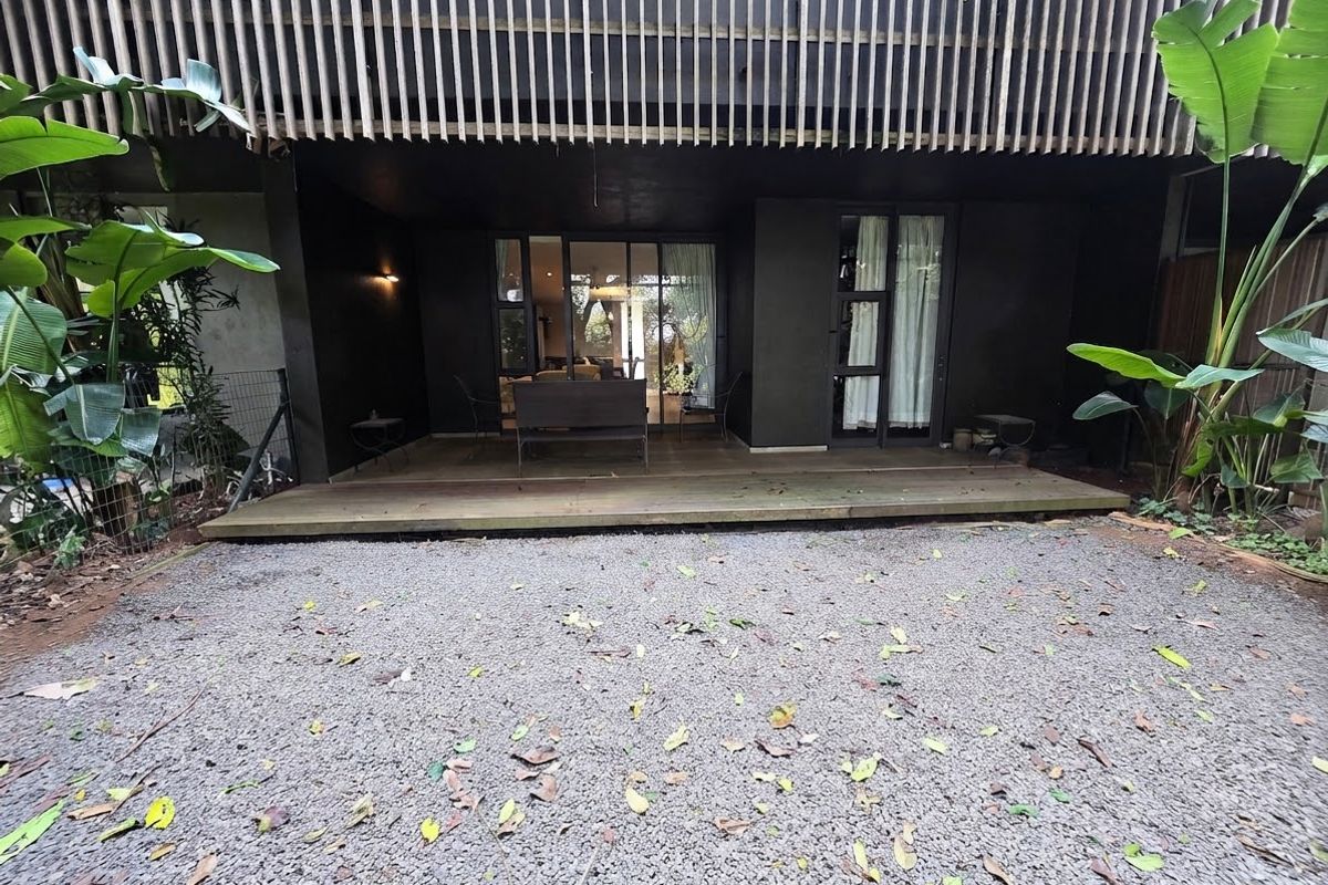 A rear exterior view featuring a timber deck, gravel courtyard, and a modern vertical timber slat screen providing privacy to the building facade.
