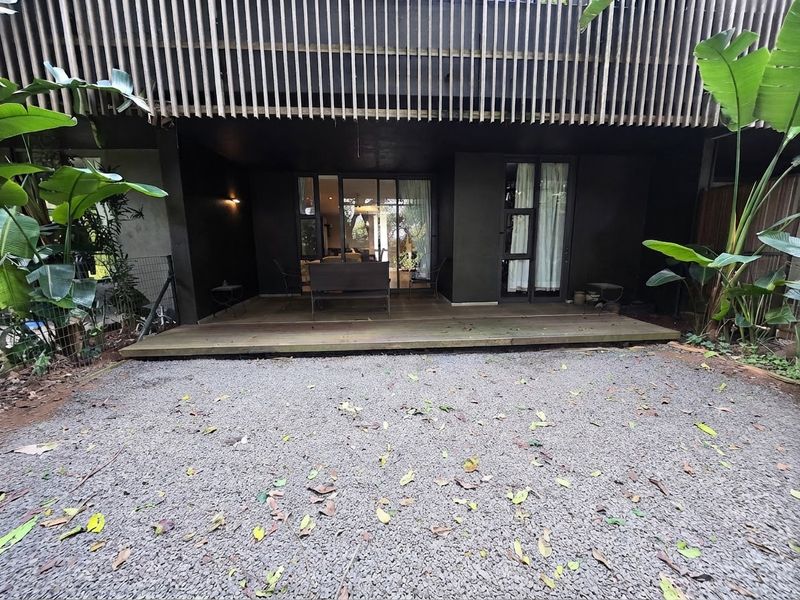 A rear exterior view featuring a timber deck, gravel courtyard, and a modern vertical timber slat screen providing privacy to the building facade.