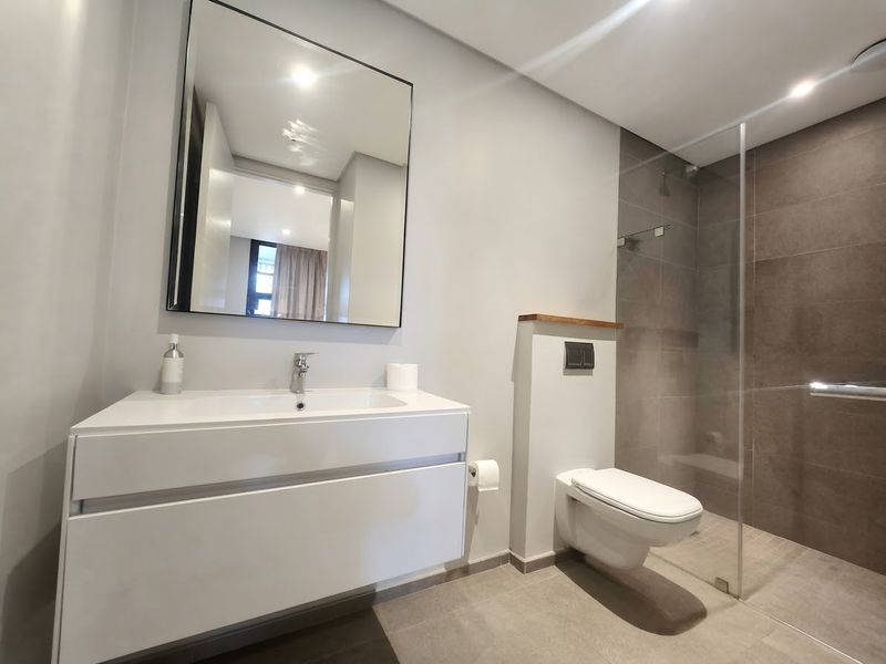 Modern bathroom featuring a wall-mounted vanity with integrated basin, wall-hung toilet with concealed cistern, and a spacious walk-in shower with glass screen.