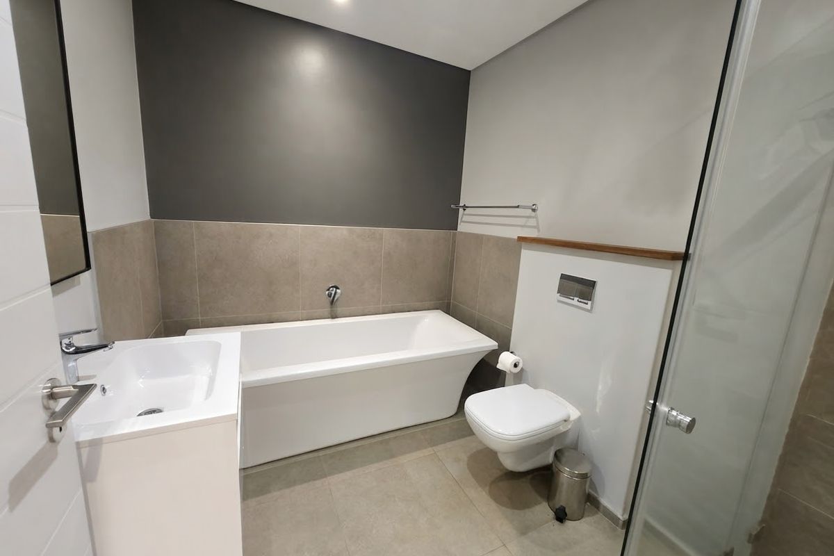 Modern bathroom featuring a sleek freestanding bathtub, wall-mounted toilet, vanity basin, and a separate glass-enclosed shower with contemporary neutral tiling.