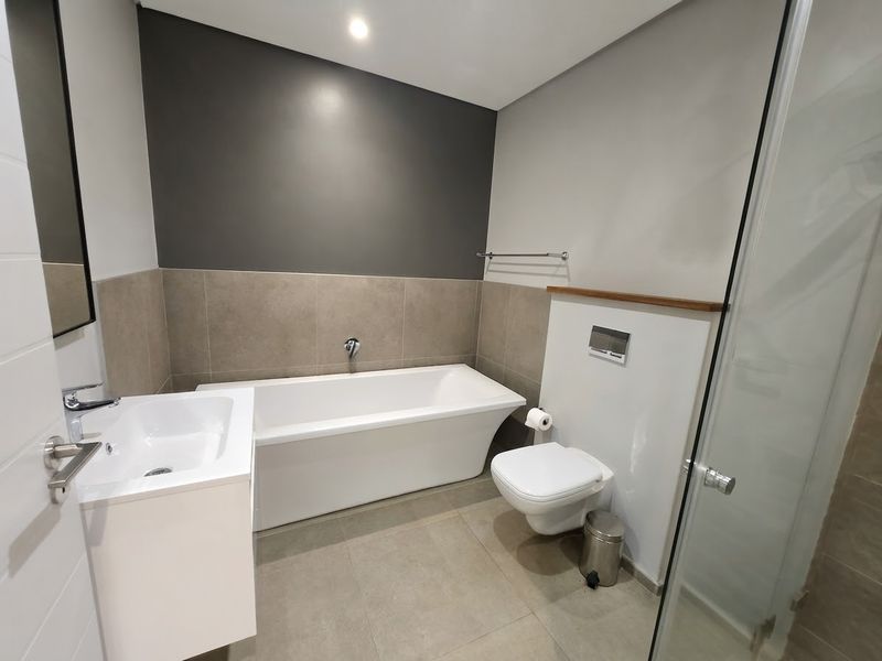 Modern bathroom featuring a sleek freestanding bathtub, wall-mounted toilet, vanity basin, and a separate glass-enclosed shower with contemporary neutral tiling.