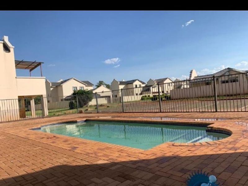 A communal swimming pool area featuring brick paving and secure metal perimeter fencing within a residential apartment complex.