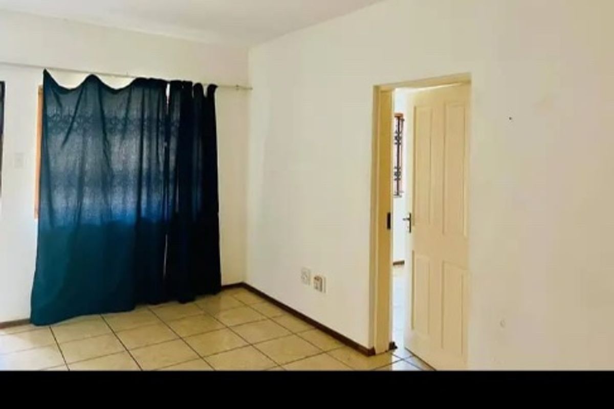An empty living room featuring ceramic floor tiles, a flush mount ceiling light, and a standard internal door.