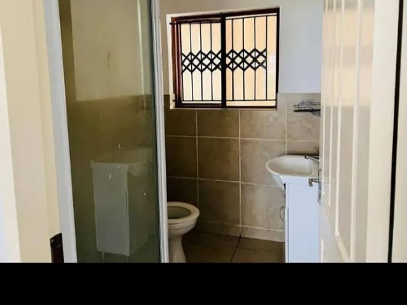 A functional bathroom featuring a shower enclosure, pedestal basin, and toilet, with tiled walls and security bars on the window.