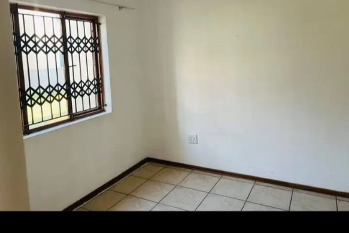 A simple, empty bedroom featuring tiled flooring and a window fitted with a security gate.
