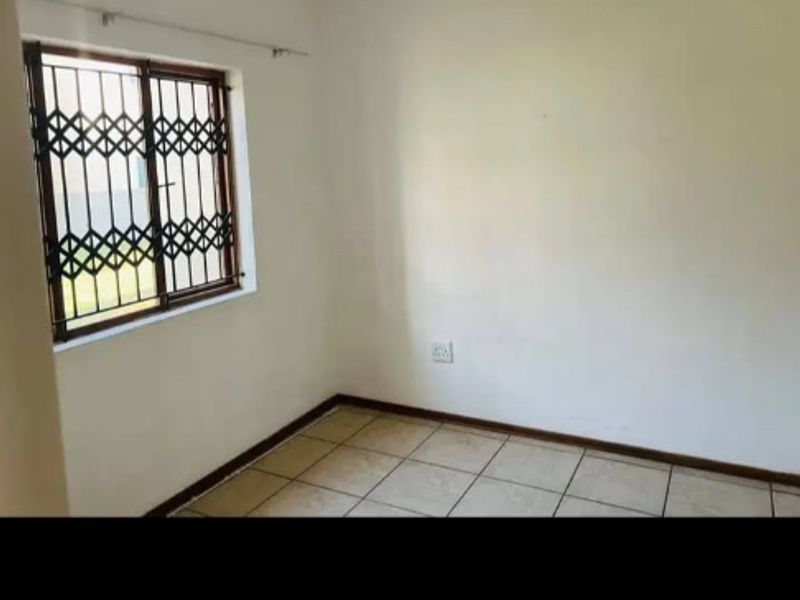 A simple, empty bedroom featuring tiled flooring and a window fitted with a security gate.
