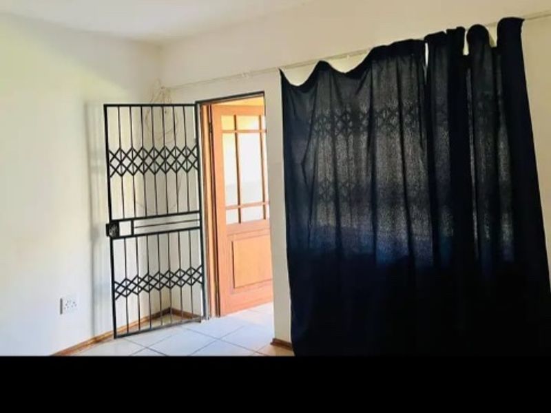An interior view of an apartment entrance featuring tiled flooring, a security gate, and a timber door leading to an exterior space.