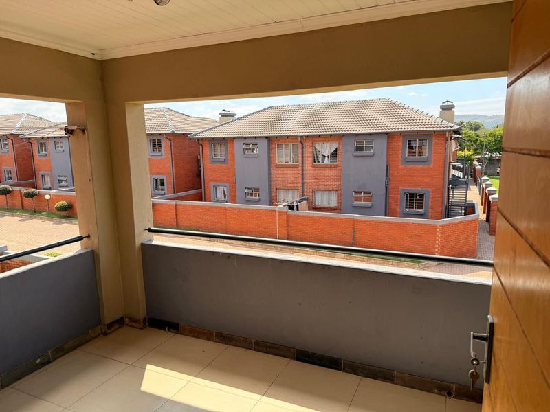 A covered balcony with tiled flooring and a metal balustrade, offering an elevated view of the surrounding townhouse complex.