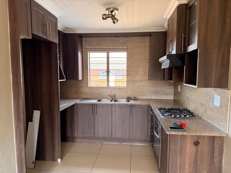 A functional kitchen featuring dark wood-look cabinetry, gas hob, built-in oven, and tiled finishes, offering a practical layout for culinary activities.