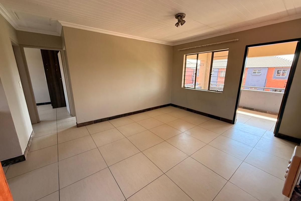 A bright, empty living room featuring neutral tiled flooring, a tongue and groove ceiling, and direct access to an outdoor balcony area.