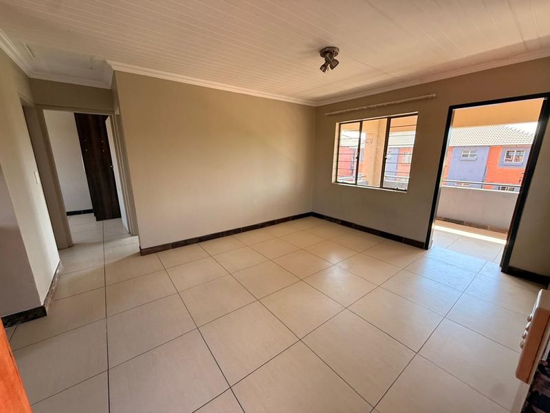 A bright, empty living room featuring neutral tiled flooring, a tongue and groove ceiling, and direct access to an outdoor balcony area.
