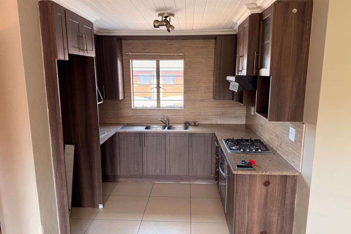 A functional kitchen featuring dark wood-finish cabinetry, laminate countertops, a gas hob with extractor, and tiled flooring, offering a practical layout for daily cooking.