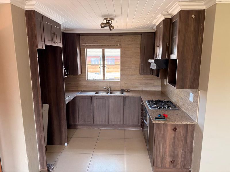 A functional kitchen featuring dark wood-finish cabinetry, laminate countertops, a gas hob with extractor, and tiled flooring, offering a practical layout for daily cooking.