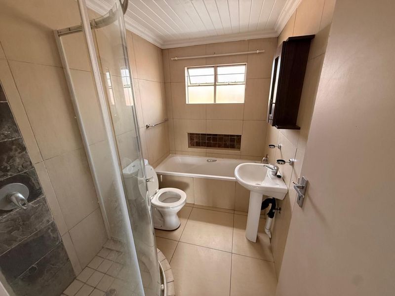 A functional bathroom featuring a shower enclosure, bathtub, pedestal basin, and toilet with neutral wall and floor tiling.