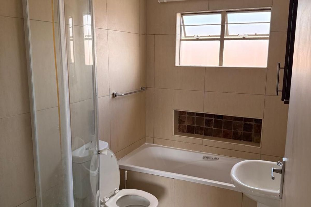 A functional bathroom featuring a shower enclosure, bathtub, pedestal basin, and toilet with neutral wall and floor tiling.